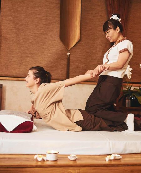 Thai masseuse sitting on woman and pulling her arms